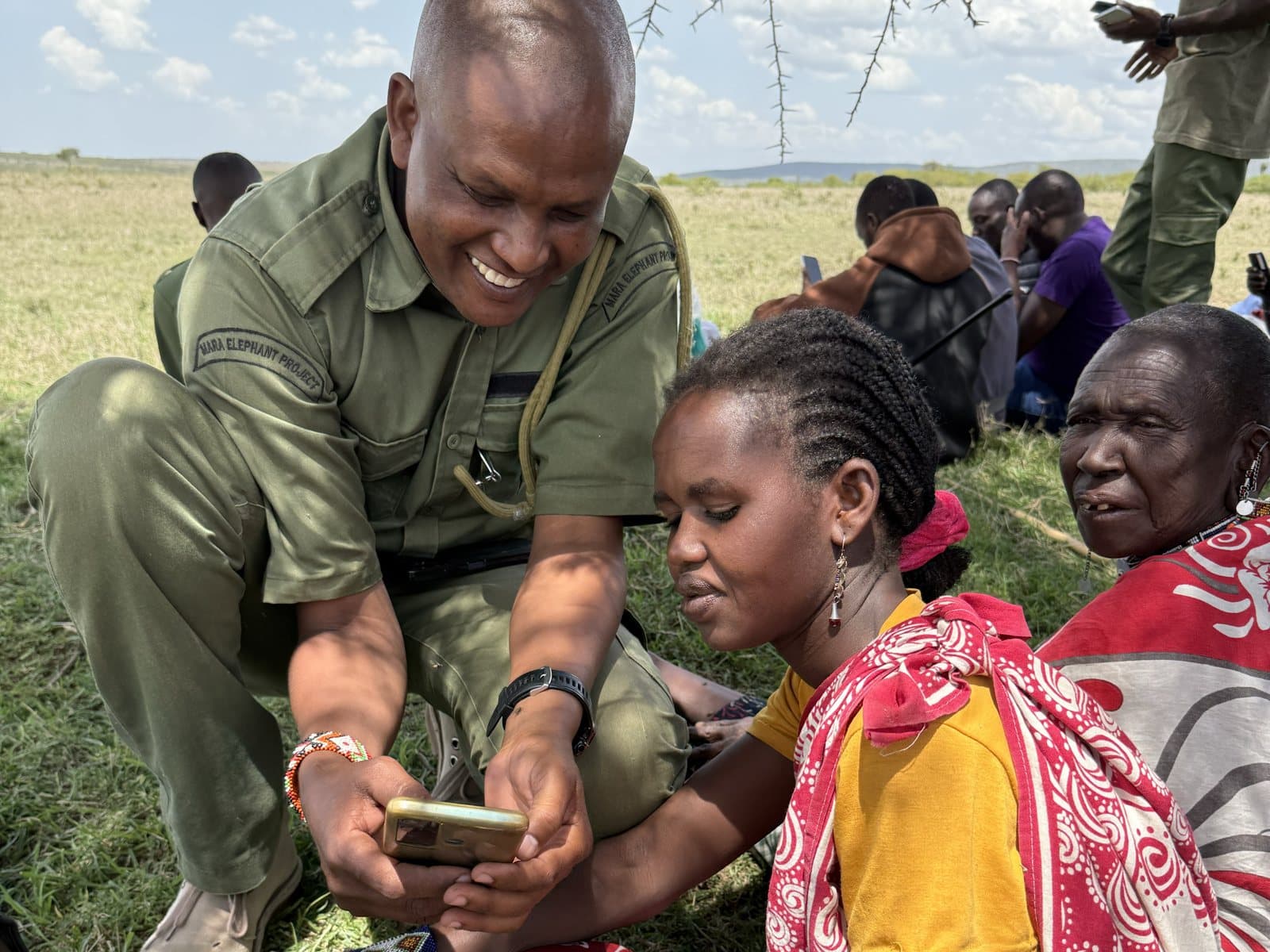 A Mara Elephant Project ranger showing a community member how to report on a phone