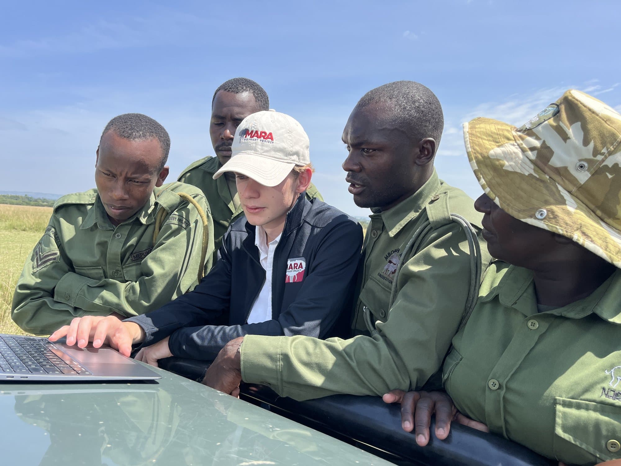 Will May showing Mara Elephant Project rangers the VirtualRanger dashboard on a laptop on the bonnet of a ranger vehicle